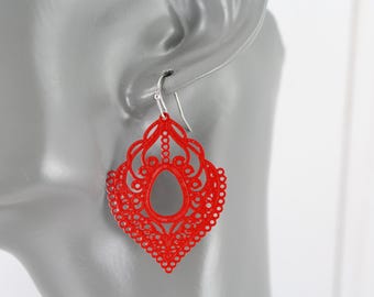 May include: Red dangle earrings with a delicate, intricate, lacy design. The earrings are shaped like a diamond with a large oval cutout in the center.