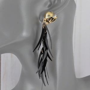 May include: Black feather-like dangle earrings with a gold clip-on closure.