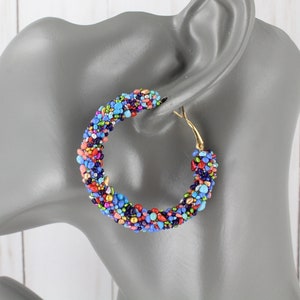 May include: A pair of large hoop earrings made of colorful beads. The beads are in shades of blue, red, pink, green, and gold. The earrings are made of a gold-toned metal.