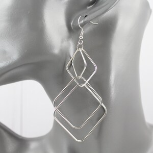 May include: A silver-toned dangle earring featuring two interconnected diamond-shaped wire frames. The smaller diamond sits above a larger diamond, both constructed from thin, polished metal wire. The earring attaches with a standard hook wire.