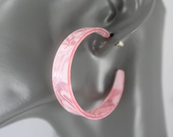 May include: A pair of pink hoop earrings with a marbled design. The earrings are a light pink color with a swirling pattern of white and darker pink. The earrings are attached to a gray ear model.
