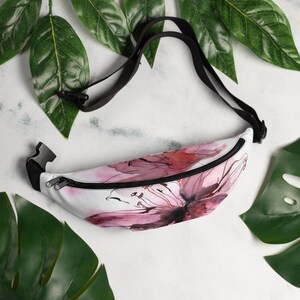 May include: A white fanny pack with a pink watercolour floral design. The fanny pack has a black adjustable strap.