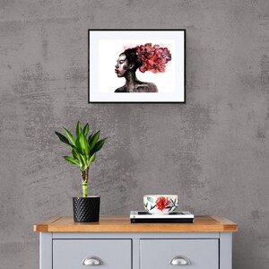 May include: A framed watercolor painting of a woman with a red floral crown. The woman is looking to the side and has dark skin. The background is white.