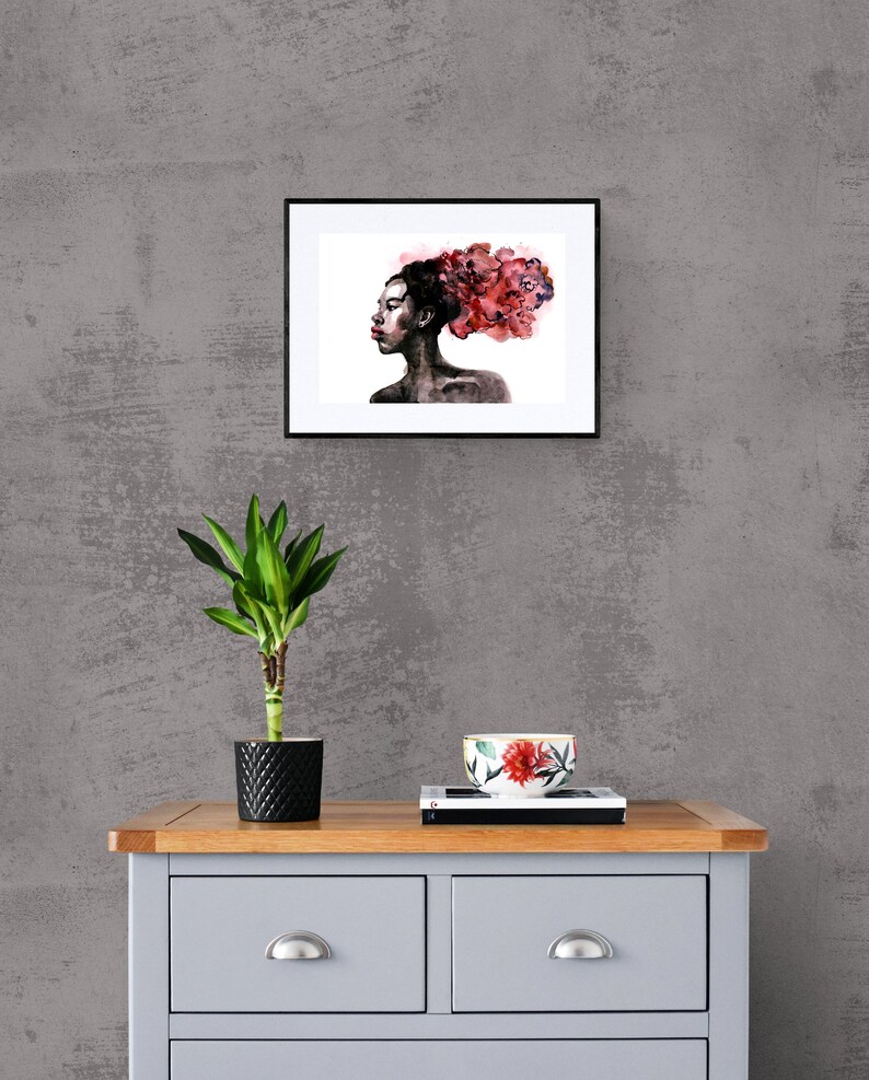 May include: A framed watercolor painting of a woman with a red floral crown. The woman is looking to the side and has dark skin. The background is white.