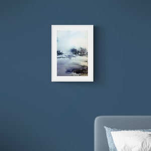 May include: A framed watercolour painting depicting a landscape. The artwork uses blues, purples, and browns to create a misty, atmospheric effect. The white frame contrasts with the dark blue wall, creating a striking visual.
