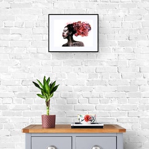 May include: A framed watercolor painting of a woman with a pink and red floral design in her hair. The painting is hanging on a white brick wall above a gray dresser with a plant in a pink pot and a floral bowl on top.