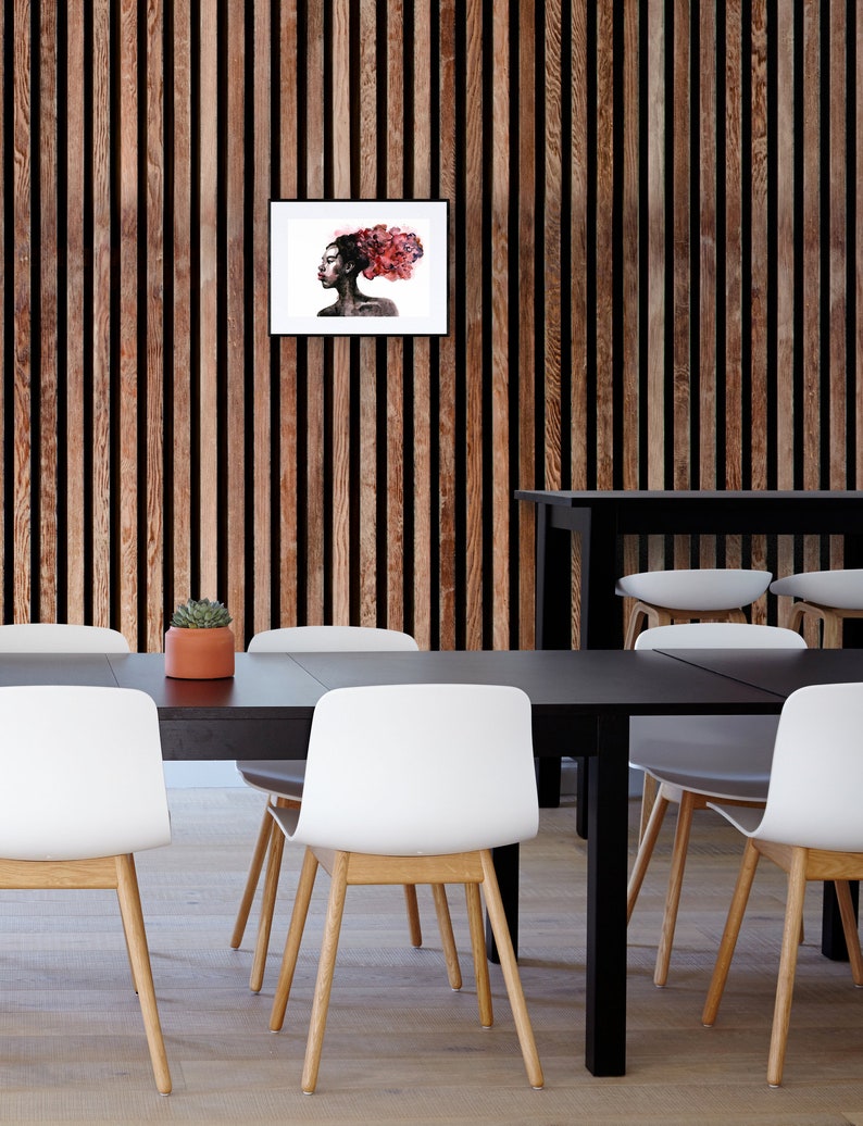 May include: A black and white framed print of a woman with red hair. The woman is looking to the side and has a serious expression. The print is hanging on a wood wall.