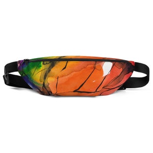 May include: A black fanny pack with a zipper closure. The fanny pack is decorated with a colourful abstract watercolour design featuring shades of orange, yellow, green, and blue.