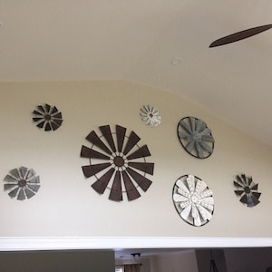 May include: A wall decor set featuring eight metal windmills in various sizes and colours, including brown, grey, and white. The windmills are arranged in a circular pattern on a white wall.