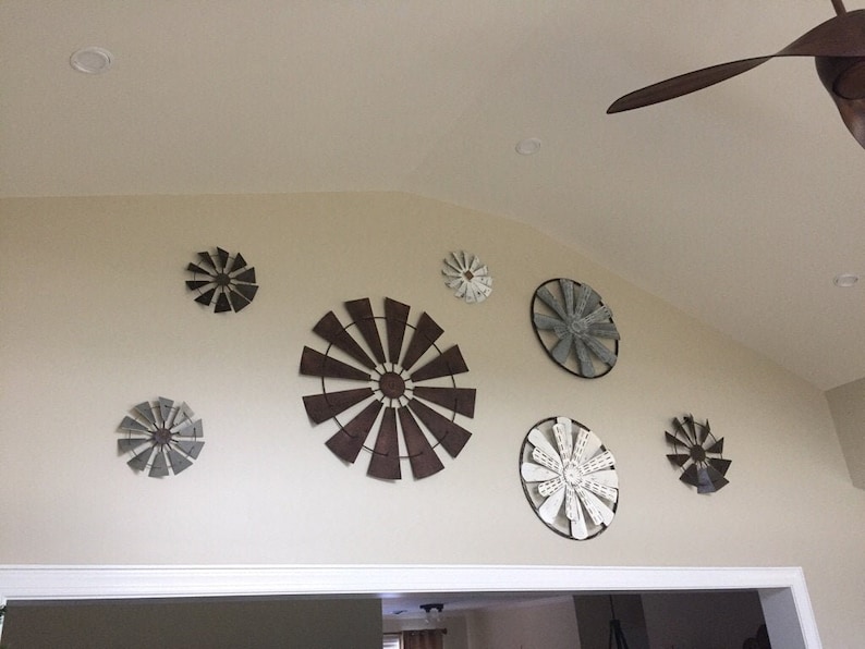 May include: A wall decor set featuring eight metal windmills in various sizes and colours, including brown, grey, and white. The windmills are arranged in a circular pattern on a white wall.