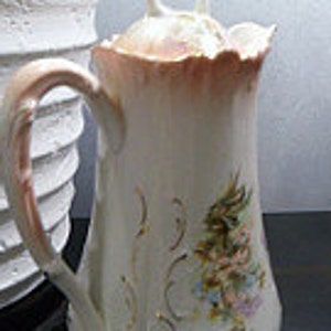 May include: A white porcelain creamer with a pink floral design and a pink handle. The creamer has a lid with a decorative knob.