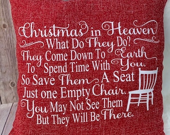 May include: Red decorative throw pillow with white text that reads "Christmas in Heaven." The pillow features a chair graphic and a heartfelt message about remembering loved ones during the holidays. The pillow is a square shape.