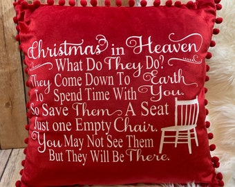 May include: Red velvet throw pillow with white pom-poms around the edges. The pillow features a white embroidered message that reads: "Christmas in Heaven What Do They Do? They Come Down To Earth To Spend Time With You. So Save Them A Seat Just One Empty Chair. You May Not See Them But They Will Be There."