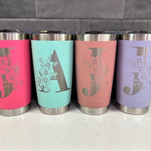 May include: Four stainless steel tumblers in pink, teal, peach, and lavender. Each tumbler has a floral design with a letter. The letters are "J", "A", and "J" and "J". The tumblers have a silver rim and base.