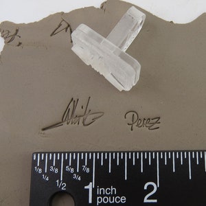 Pu&ograve; includere: Un timbro rettangolare trasparente con un design strutturato poggia su un pezzo di argilla. L'argilla &egrave; contrassegnata dalle firme "Whit" e "Perez". Un righello mostra le misure in pollici.