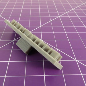 May include: A gray plastic 3D printed object with a rectangular base and a flat, rectangular top with a series of small, rectangular holes.