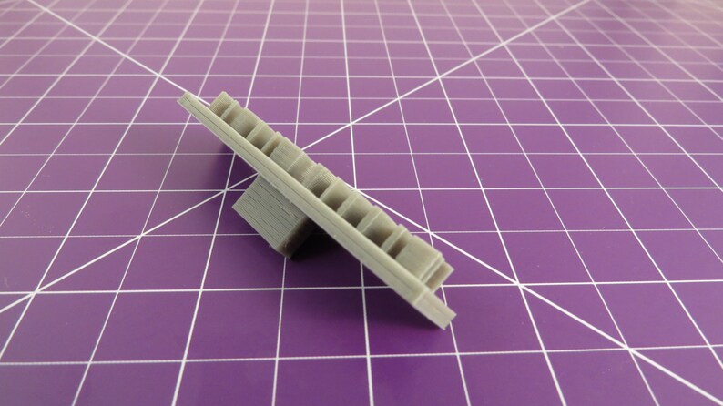 May include: A gray plastic 3D printed object with a rectangular base and a flat, rectangular top with a series of small, rectangular holes.