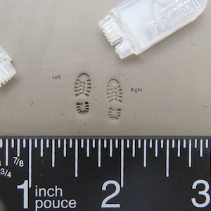 May include: Close-up of two shoe prints in clay, one labeled "Left" and the other "Right". A ruler is visible below the prints, with markings in inches. The prints are approximately 1 inch long.