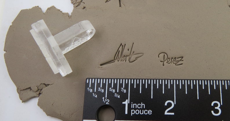 Pu&ograve; includere: Uno strumento di argilla in plastica trasparente con un manico e una testa rettangolare, accanto a un righello che mostra pollici. Lo strumento &egrave; su una superficie di argilla grigia con le firme "Witte" e "Perez" impresse.