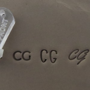 May include: A clear plastic stamp with the word "FRONT" printed on it. The stamp is used to create impressions of the letters "CG" in clay. The letters are shown in four different styles.