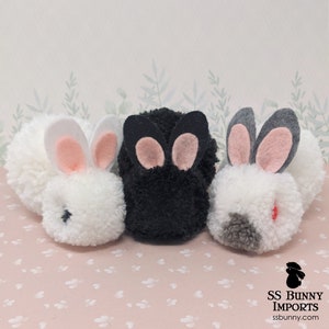 May include: Three pom-pom bunny ornaments, one white, one black, and one gray with a red nose. The bunnies have pink felt ears and black eyes.