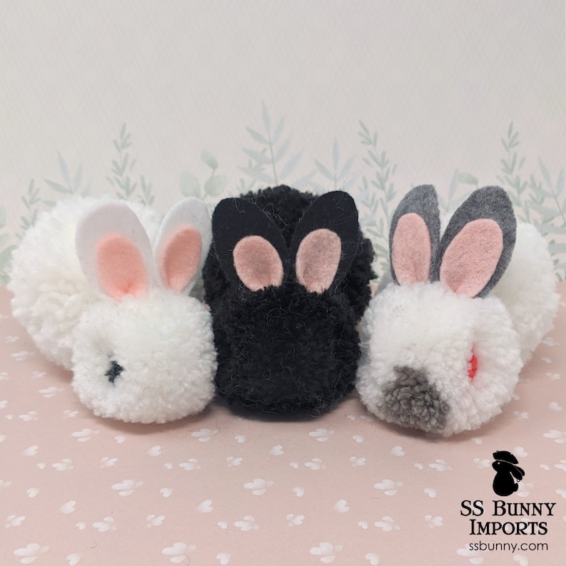 May include: Three pom-pom bunny ornaments, one white, one black, and one gray with a red nose. The bunnies have pink felt ears and black eyes.
