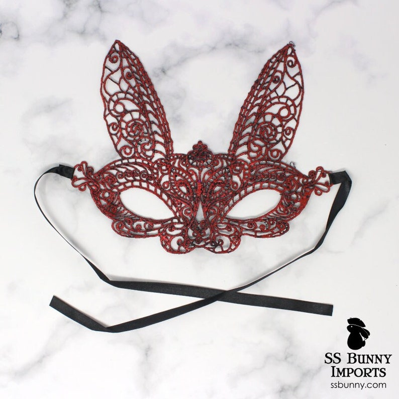 May include: Red lace bunny mask with black ribbon ties. The mask has a delicate, intricate design.
