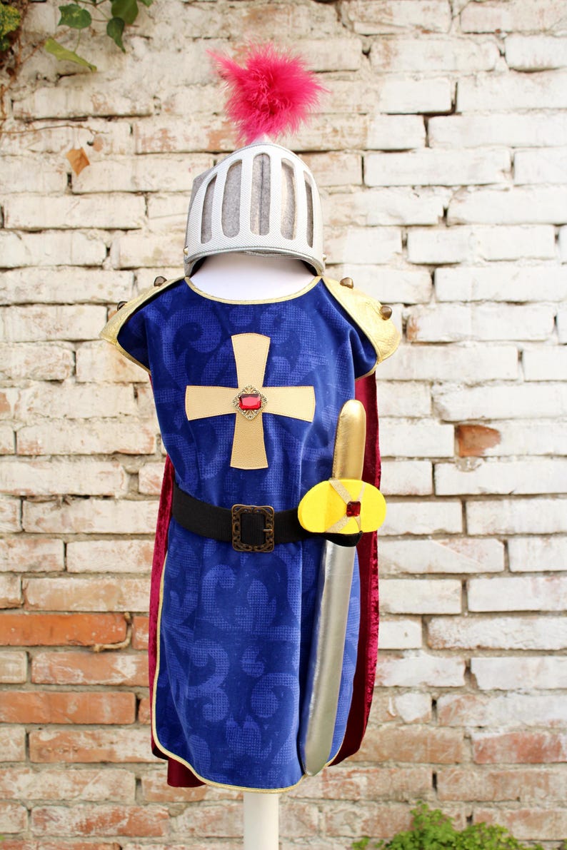 Pode incluir: Uma t&uacute;nica de veludo azul com uma cruz dourada e gema vermelha, com detalhes dourados nos ombros, cinto preto e capa vermelha. Inclui um capacete prateado com pluma rosa e uma espada prateada com punho dourado e gema vermelha incrustada.
