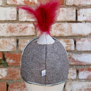 May include: A gray felt helmet with a silver trim and a red feather on top. The helmet has a small white label with the text "323" on it.