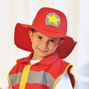 May include: A child wearing a red firefighter costume with a yellow star on the hat. The costume includes a red vest with yellow and gray reflective stripes.