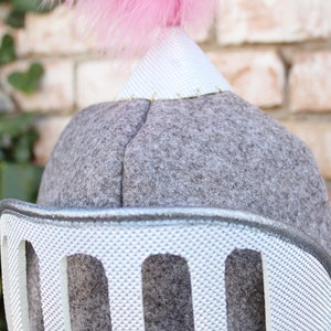 May include: A gray felt knight helmet with a silver plastic face guard and a pink feather plume on top.