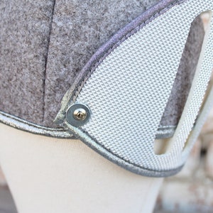 May include: A gray felt helmet with a silver trim and a silver textured panel. The helmet has a metal button on the side.