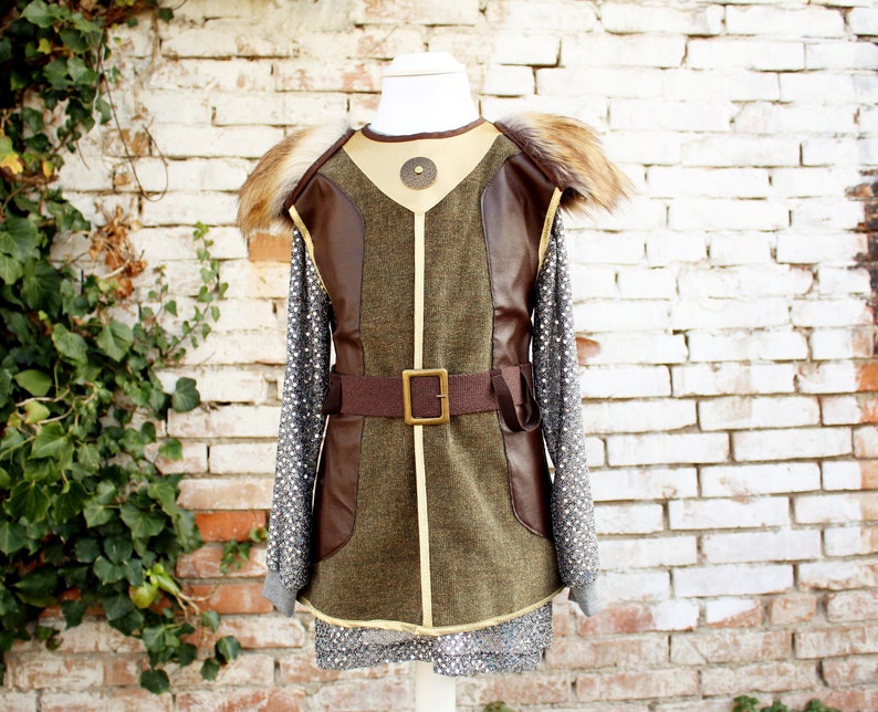 May include: A brown and green faux leather vest with a fur collar and a brown belt with a metal buckle. The vest has a decorative metal piece on the front.