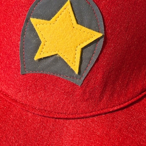May include: Red felt hat with a black felt star patch. The star is yellow and has stitching around the edges.