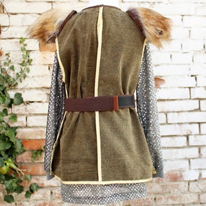 May include: A brown and green costume with a fur collar and a brown belt. The costume is on a white mannequin against a white brick wall.