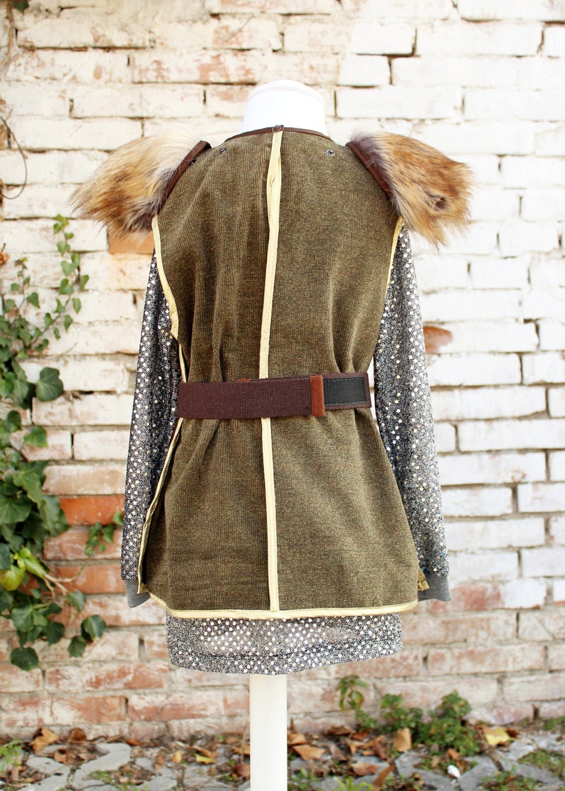 May include: A brown and green costume with a fur collar and a brown belt. The costume is on a white mannequin against a white brick wall.