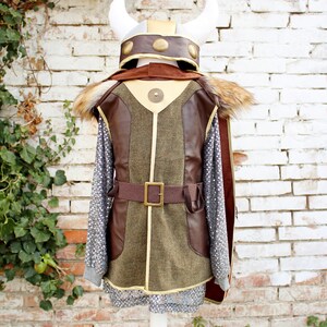 May include: A brown and green costume with a faux fur collar and a gold belt. The costume includes a helmet with horns and gold accents.