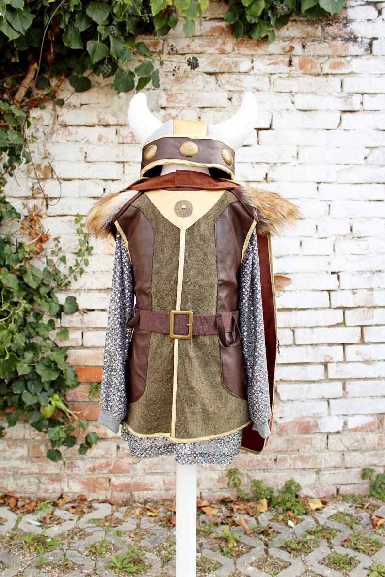 May include: A brown and green costume with a faux fur collar and a gold belt. The costume includes a helmet with horns and gold accents.