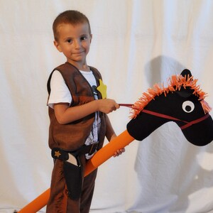 May include: A hobby horse with a black fabric head, orange yarn mane, and a long orange foam pole. The horse features a red bridle and white circular eyes. It is paired with a brown vest and pants set, including a holster and a yellow star badge.