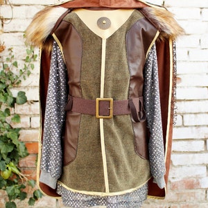 May include: A brown and green costume with a fur collar and a brown belt with a gold buckle. The costume has a gold trim and a chainmail shirt underneath.