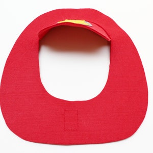 May include: Red felt bib with a yellow and gray felt design on the top. The bib has a velcro closure on the back.