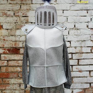 Puede incluir: Un disfraz de cota de malla plateado con un casco y una armadura a juego. El casco tiene una pluma azul en la parte superior. El texto "chainmail + armor + helmet" est&aacute; escrito en amarillo en el lado derecho de la imagen. El texto "tunica argentata + armatura + elmo" est&aacute; escrito en negro en el lado izquierdo de la imagen.