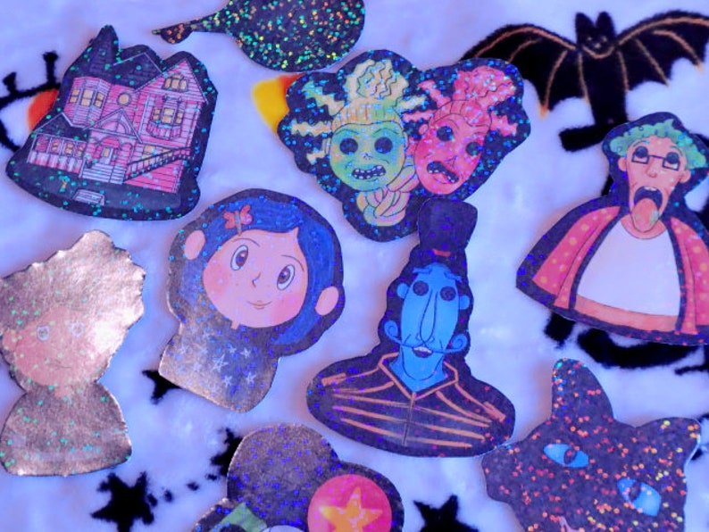 May include: A collection of nine glittery iron-on patches featuring various characters and designs, including a house, a girl with a blue bow, a blue creature with a mustache, a woman with glasses, and a black cat.