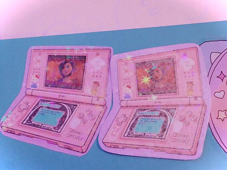 Op de afbeelding: Twee roze en witte Nintendo DS-gameconsole stickers met een cartoon afbeelding van een meisje op het scherm. De stickers hebben de tekst "START" en "SELECT" onderaan.