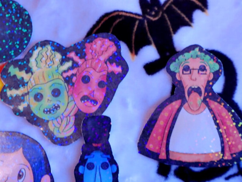 May include: Five holographic stickers featuring cartoon characters with exaggerated features. The characters are green, pink, blue, and white with black outlines. The stickers are on a white fuzzy surface.