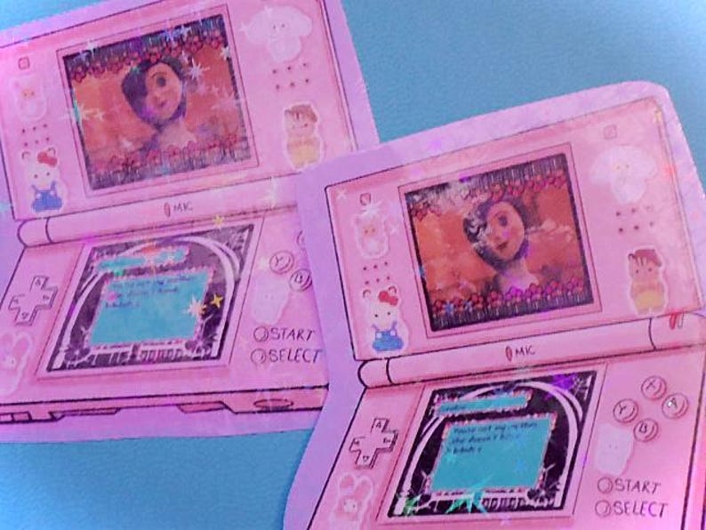 Op de afbeelding: Twee roze handheld gaming-apparaten met een cartoonfiguur op het scherm. De apparaten zijn roze en wit met een zwarte omtrek. Het scherm toont een cartoonfiguur tegen een blauwe achtergrond. De apparaten hebben knoppen met de tekst "Start" en "Select".