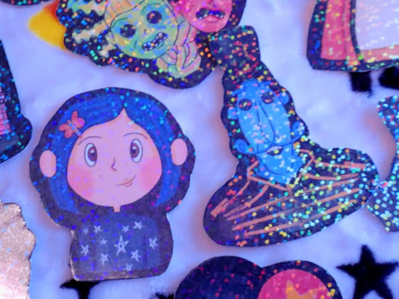 May include: A set of colorful, glittery stickers featuring characters from the movie "Coraline". The stickers feature Coraline, the Other Mother, and the cat. The stickers are perfect for adding a touch of whimsy to your laptop, water bottle, or planner.