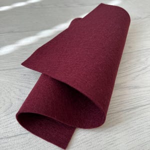 Könnte beinhalten: Ein Stück burgunderfarbenes Filzgewebe, das in der Hälfte gefaltet ist. Der Filz ist glatt und hat eine leichte Textur.