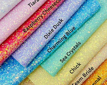 May include: A collection of glitter fabric samples in various colors, including white, pink, red, purple, blue, and yellow. Each sample is labeled with a name such as "Pretty Magical" and "Raspberry Cheesecake". The fabrics have a sparkly, textured appearance.