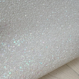 Puede incluir: Tela blanca con purpurina iridiscente y superficie texturizada.
